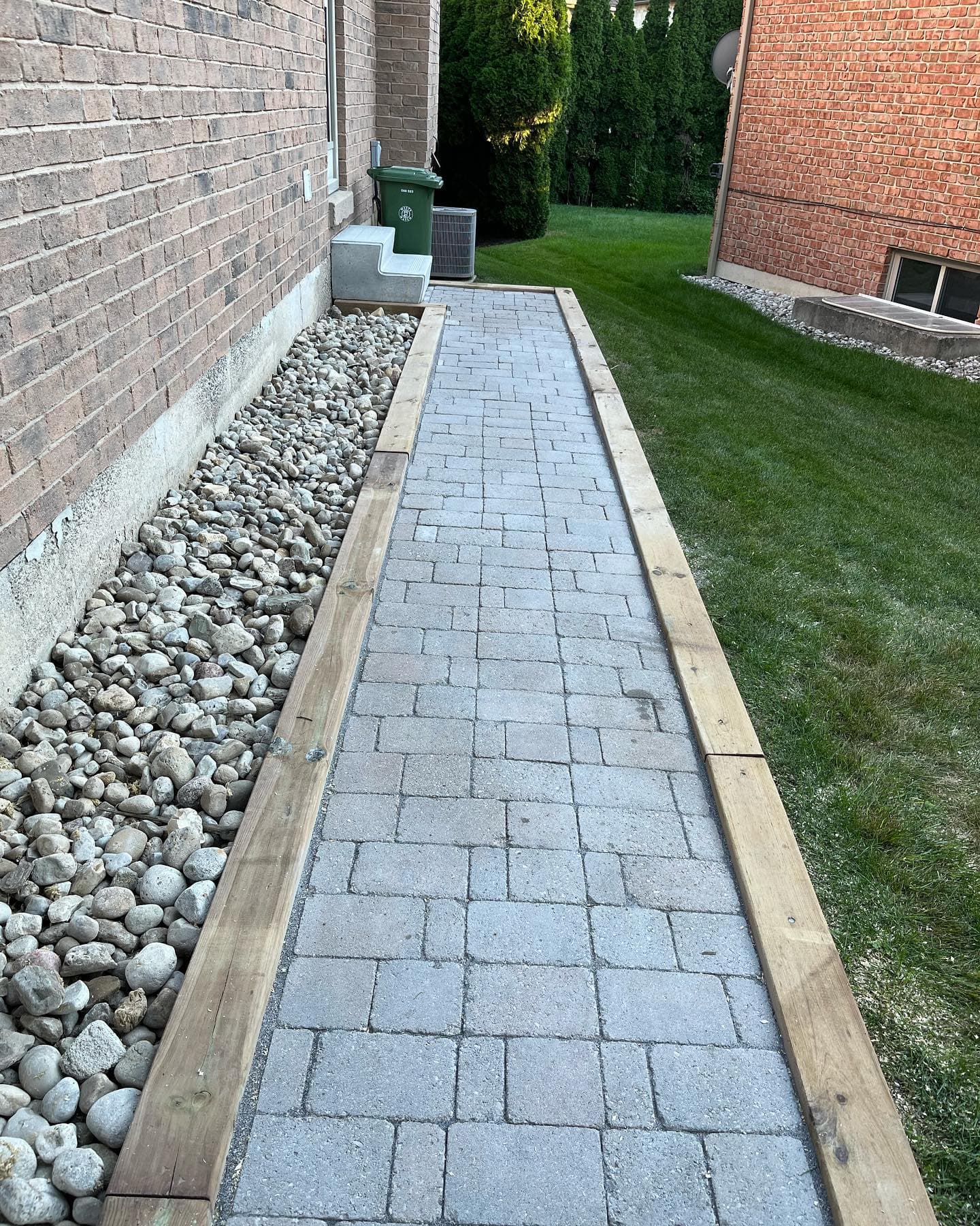 Finished paver walk with stone border alongside a brick house